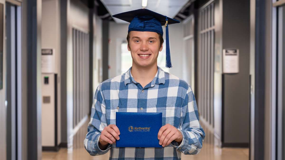 Mike smiling while wearing his graduation cap and holding his diploma.