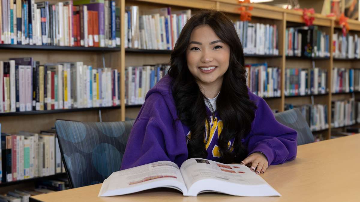 Samyris seated at a library table with a textbook open in front of her