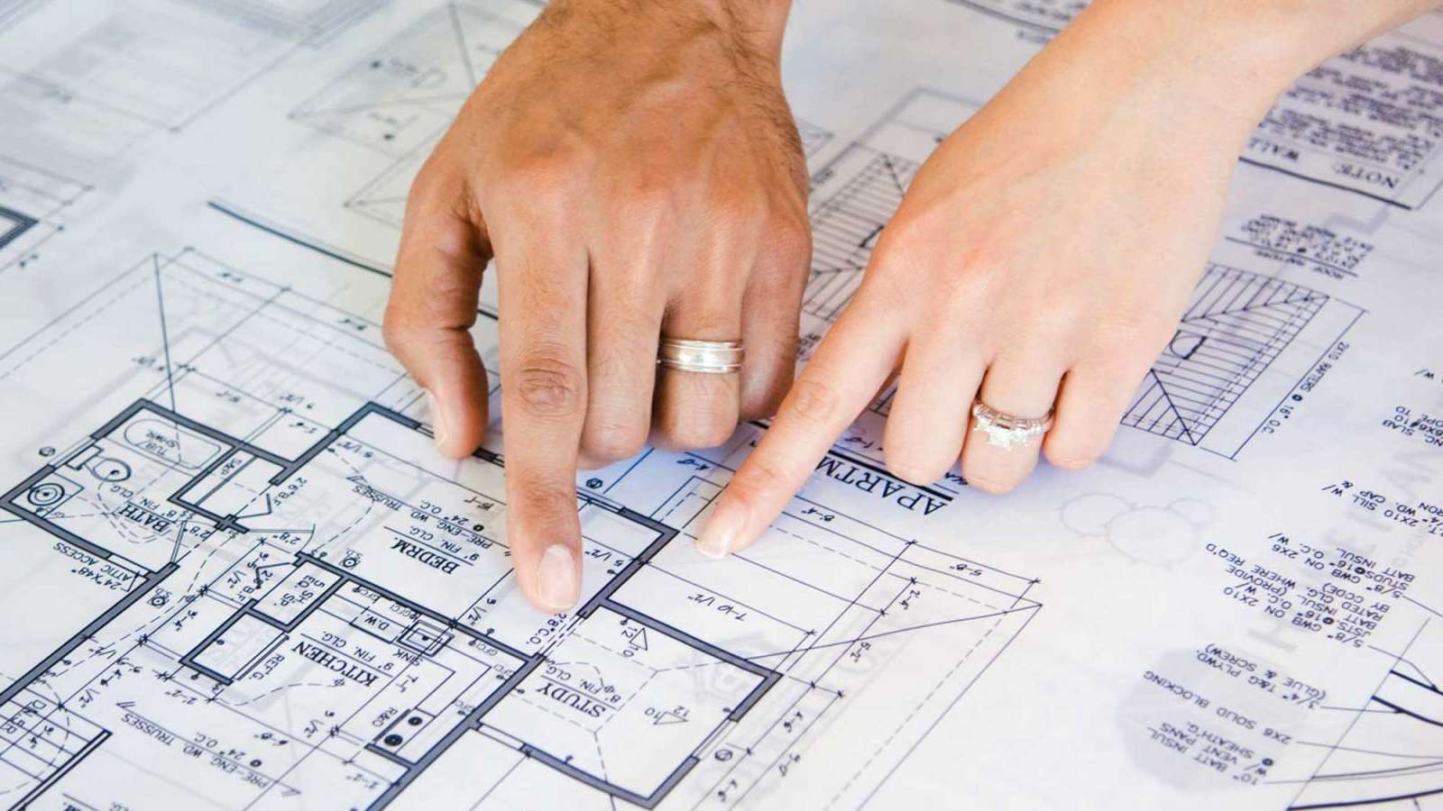 Two people point at a bedroom in blueprints.