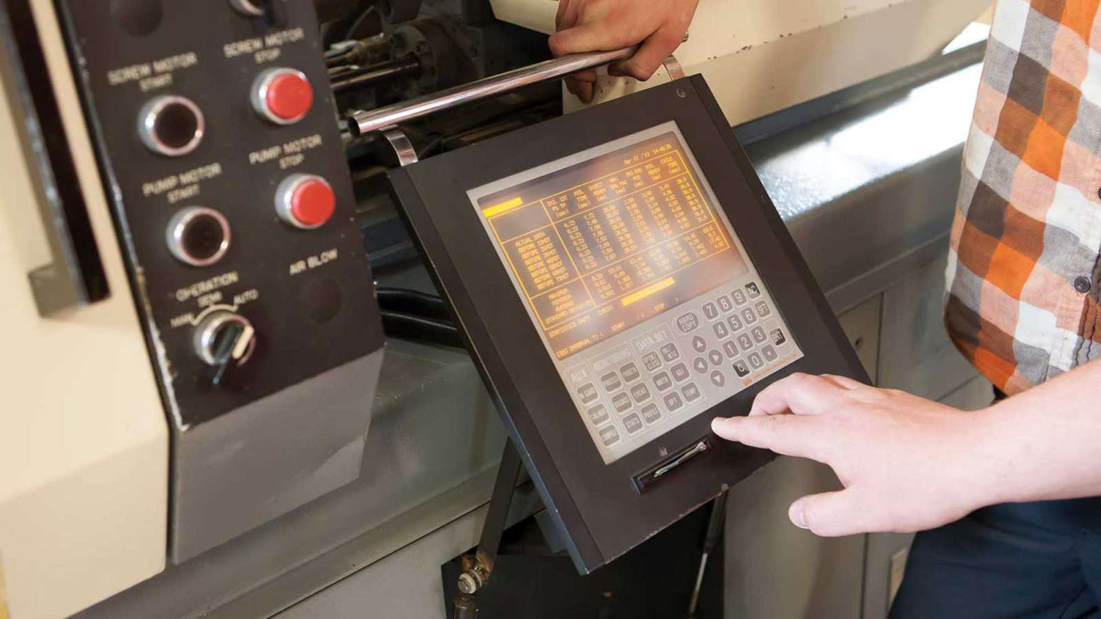 An employee looks at a display on a piece of machinery in a manufacturing plant.