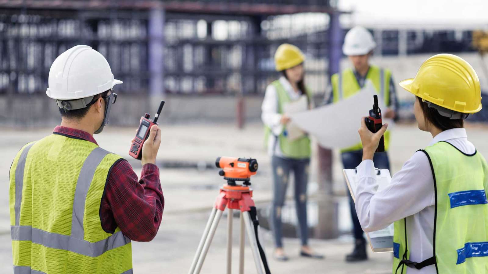 A crew standing at a worksite, examining blueprints and communicating via walkie talkies.