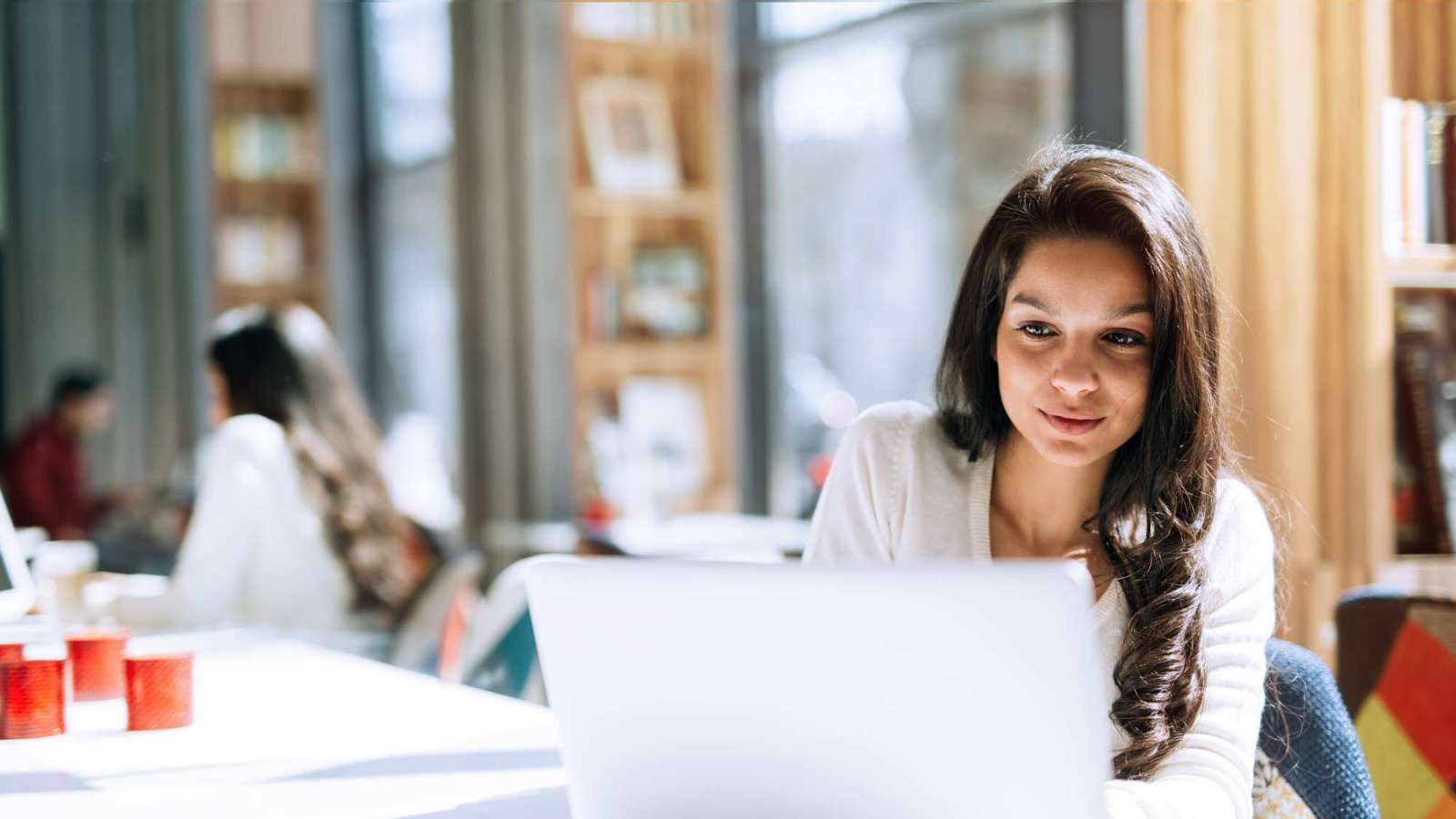 A young professional woman sitting at a table with a laptop in front of her.