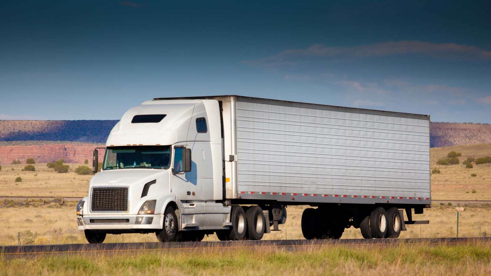 A semi truck driving on the highway through the countryside.