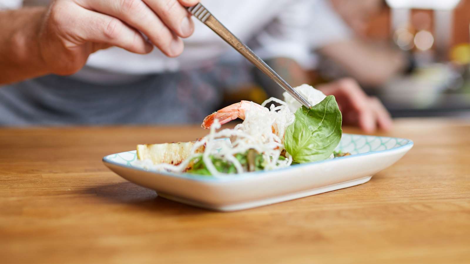 A professional chef plating an Asian dish in a restaurant kitchen.