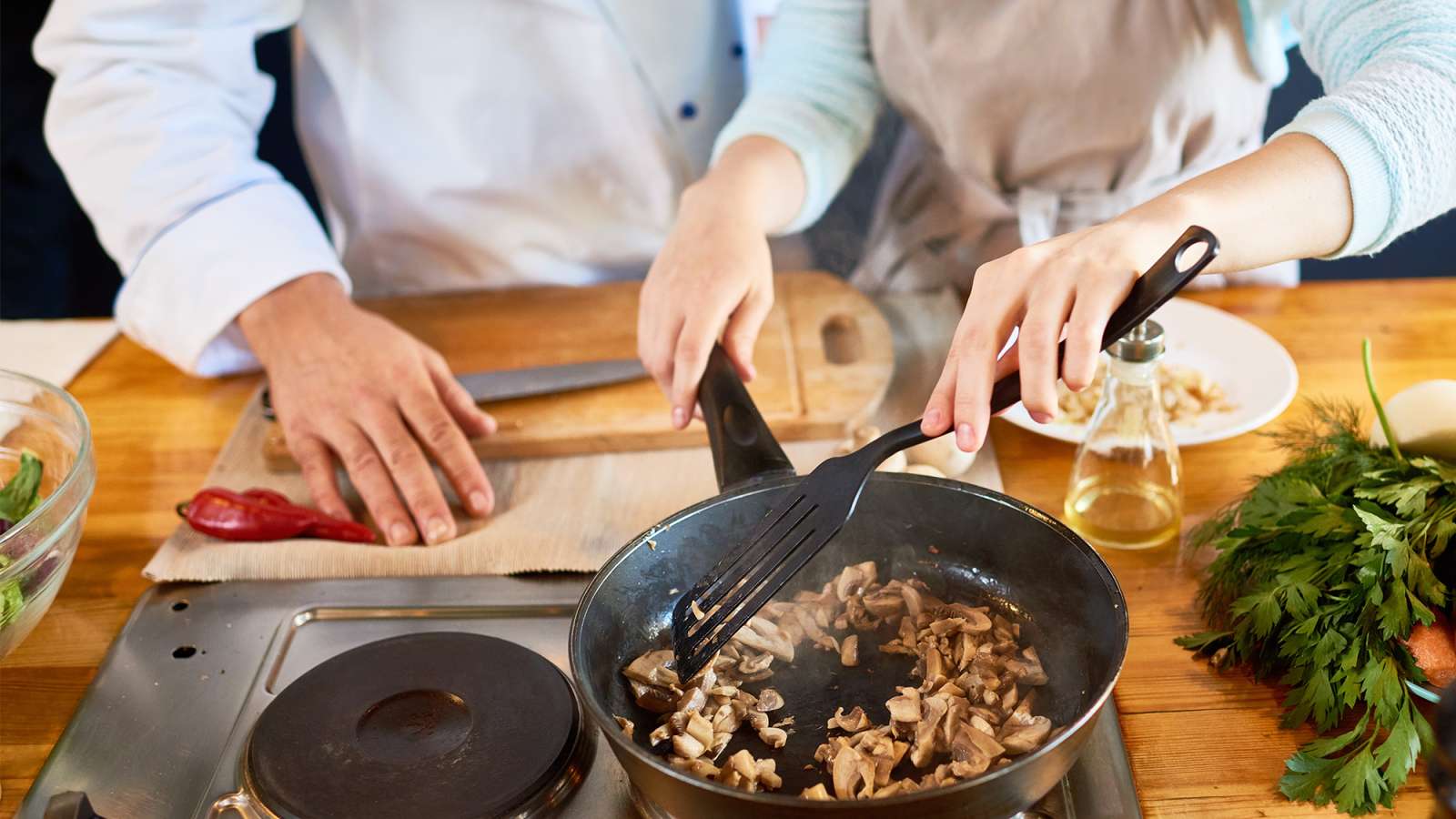 A culinary assistant is frying mushrooms under the supervision of a professional chef.