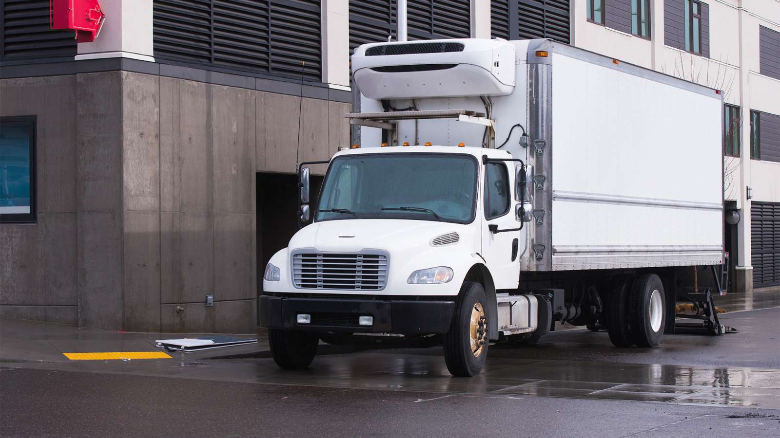 A white colored straight truck is parked on the side of the road for a delivery.