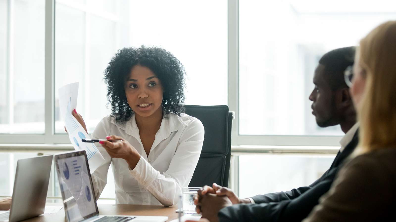 Businesswoman showing a statistics report and explaining advantages to clients at a negotiations meeting.