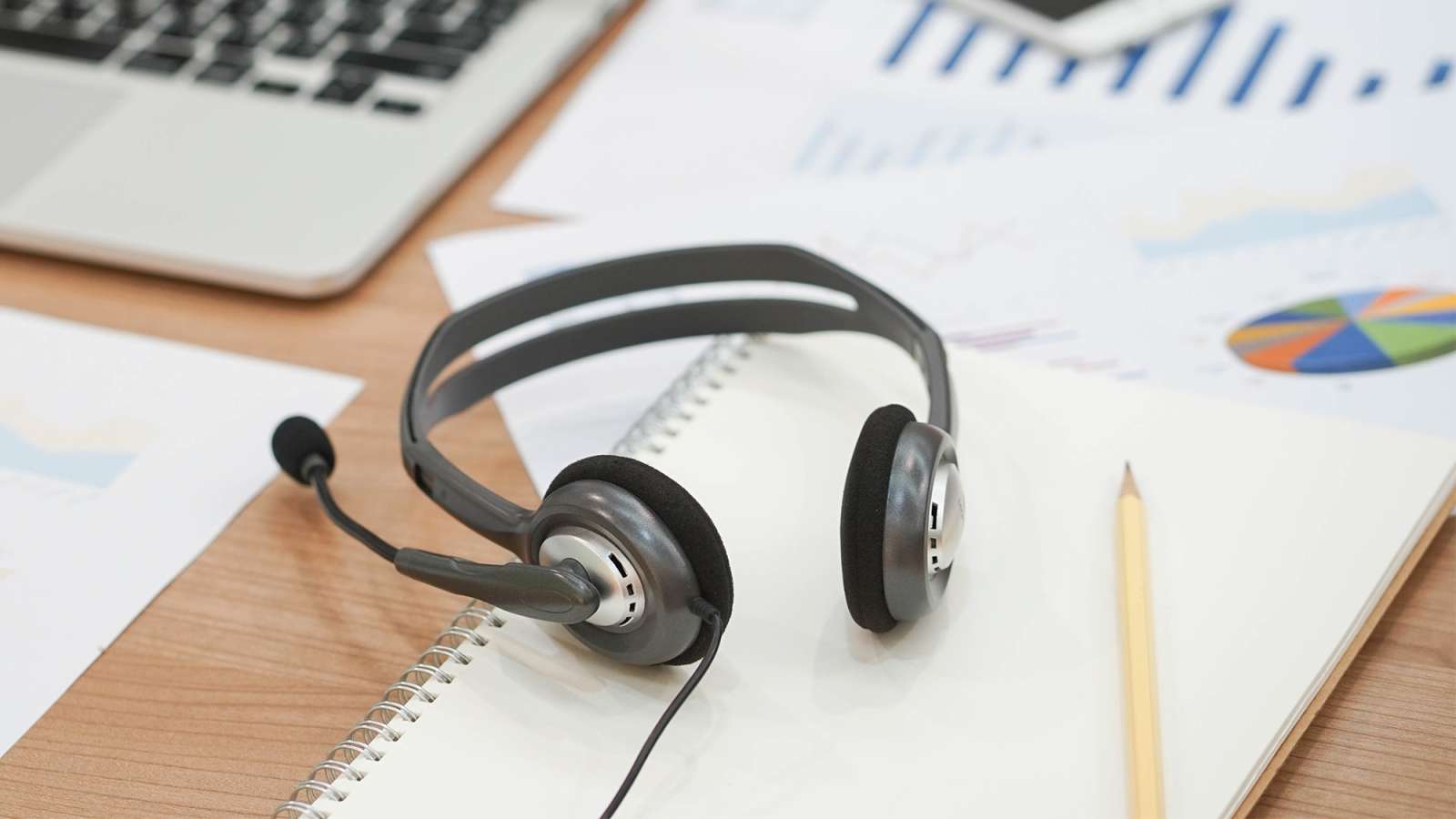 Close up of a computer headset at an office desk with laptop and documents.