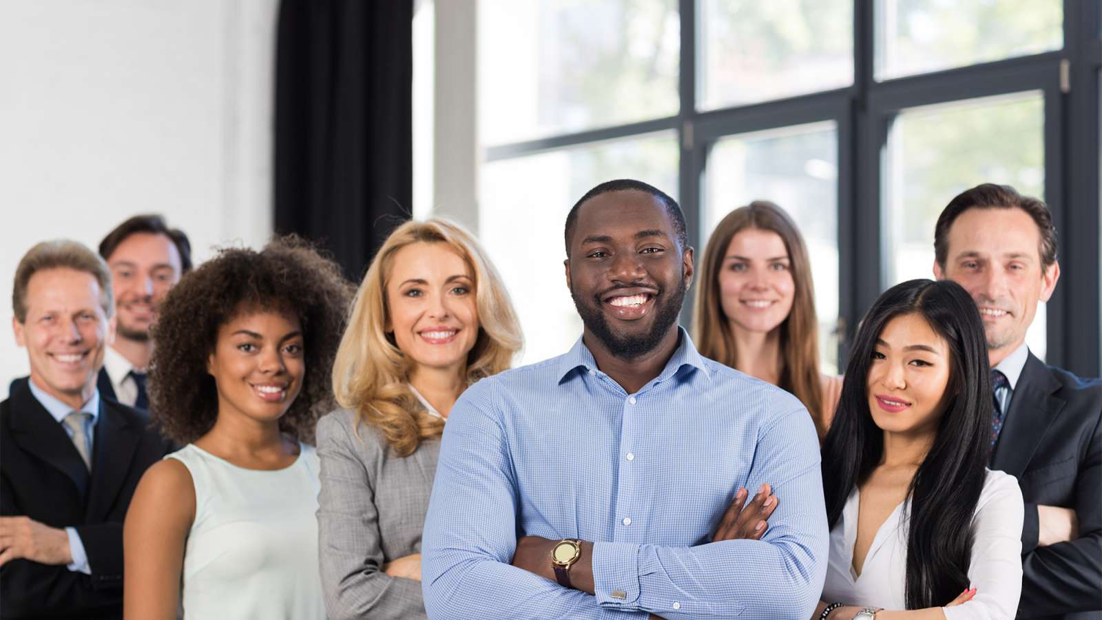 Managers and employees at a company stand together smiling.