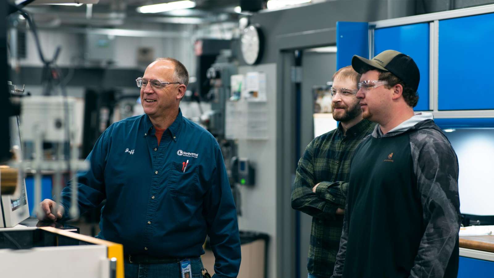 An instructor with two apprentices in a shop setting.