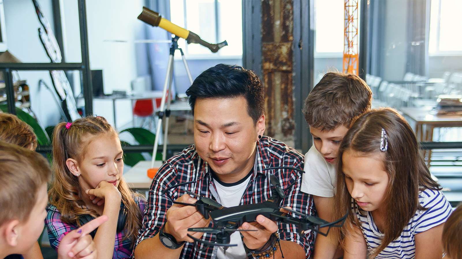 A young creative teacher is holding a helicopter model and explaining how it works to young students.