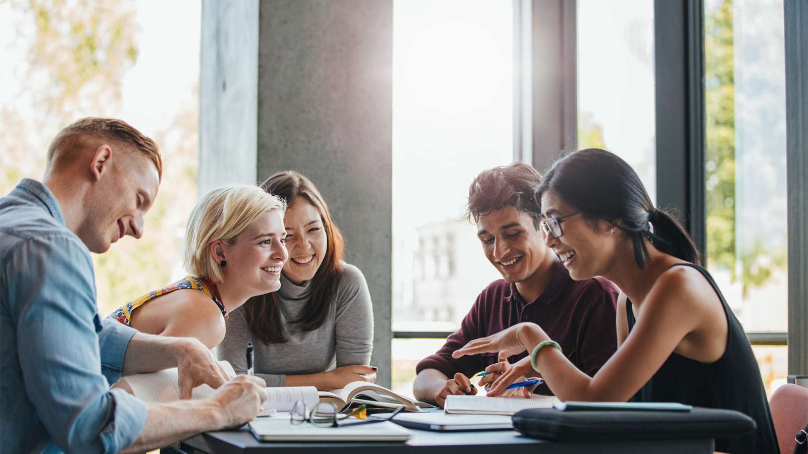 Five students are sitting at a table studying and socializing with each other.