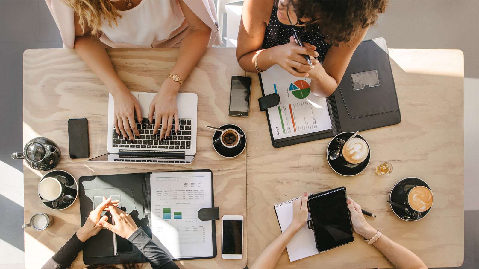 Group of women working together in a coffee shop on marketing material.