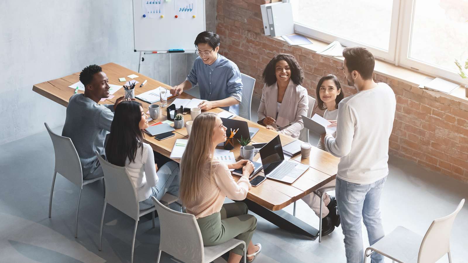 Several employees are sitting at a table in a meeting listening to a manager give a presentation.