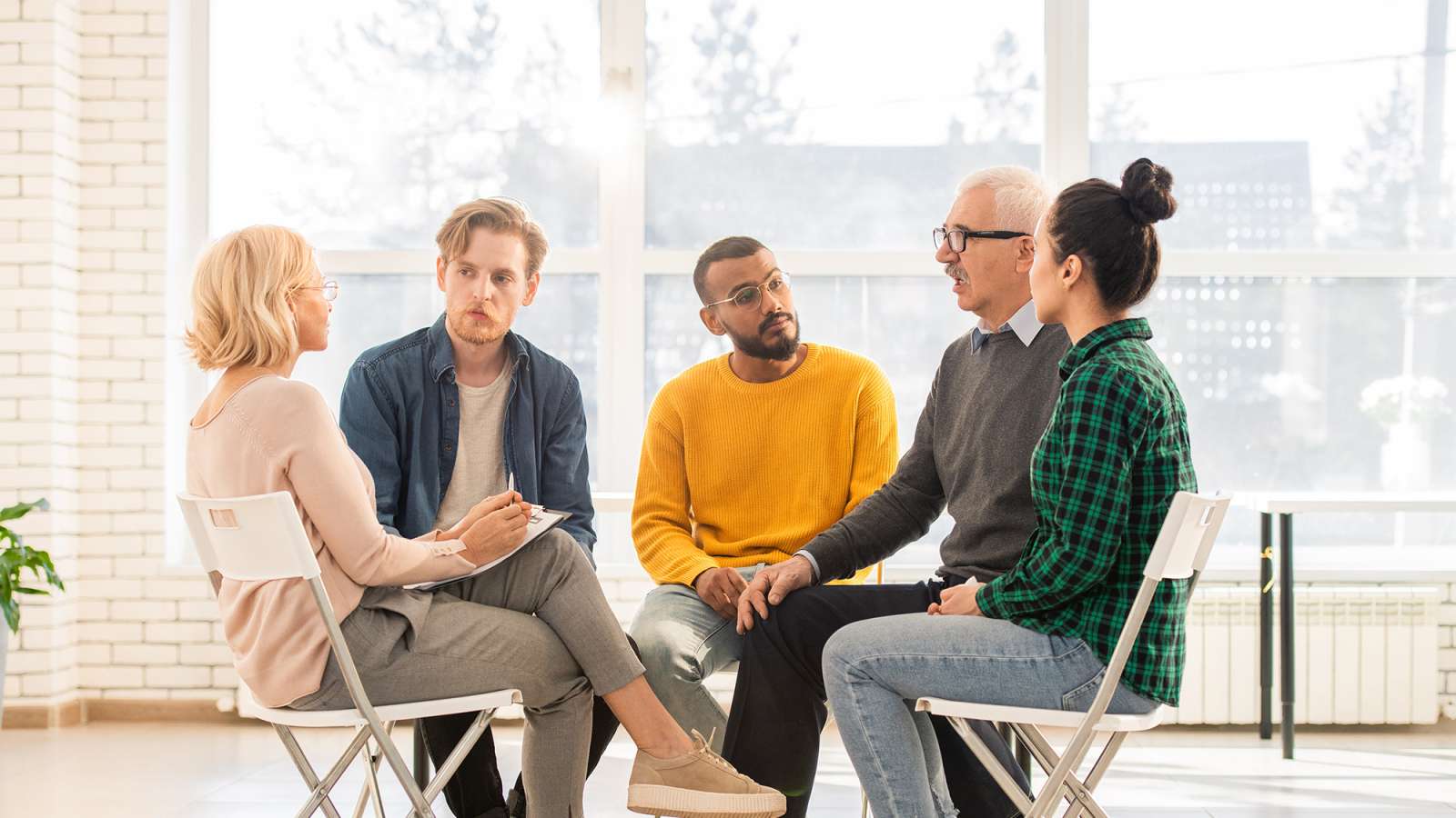 A counselor sits with a group, clipboard in hand, discussing issues in their lives.
