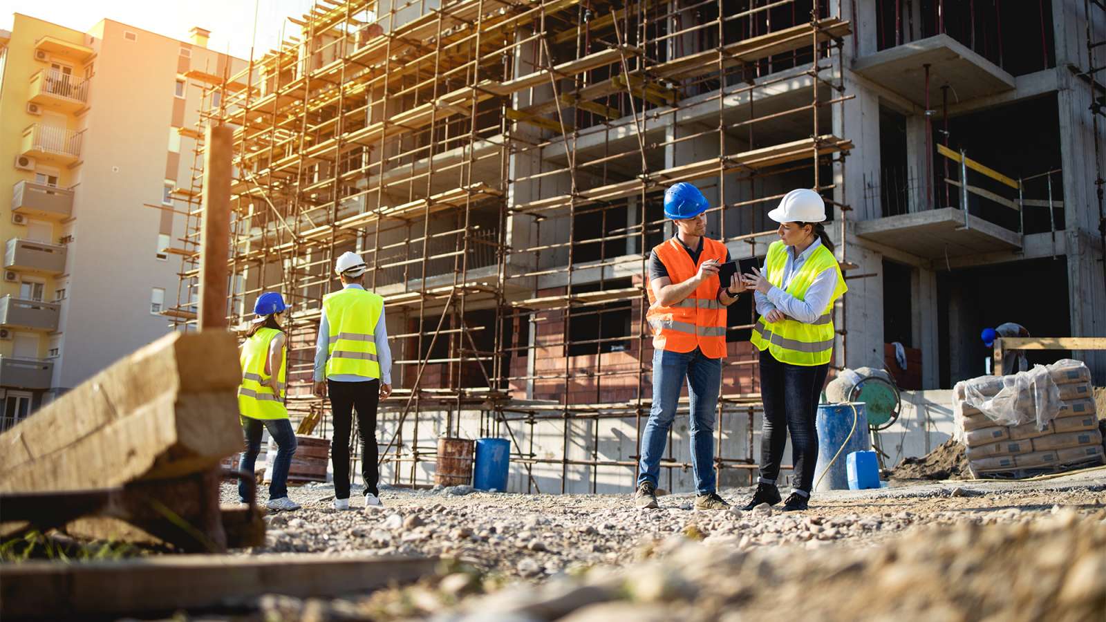 Four construction workers stand outside of a three story building that is under construction.