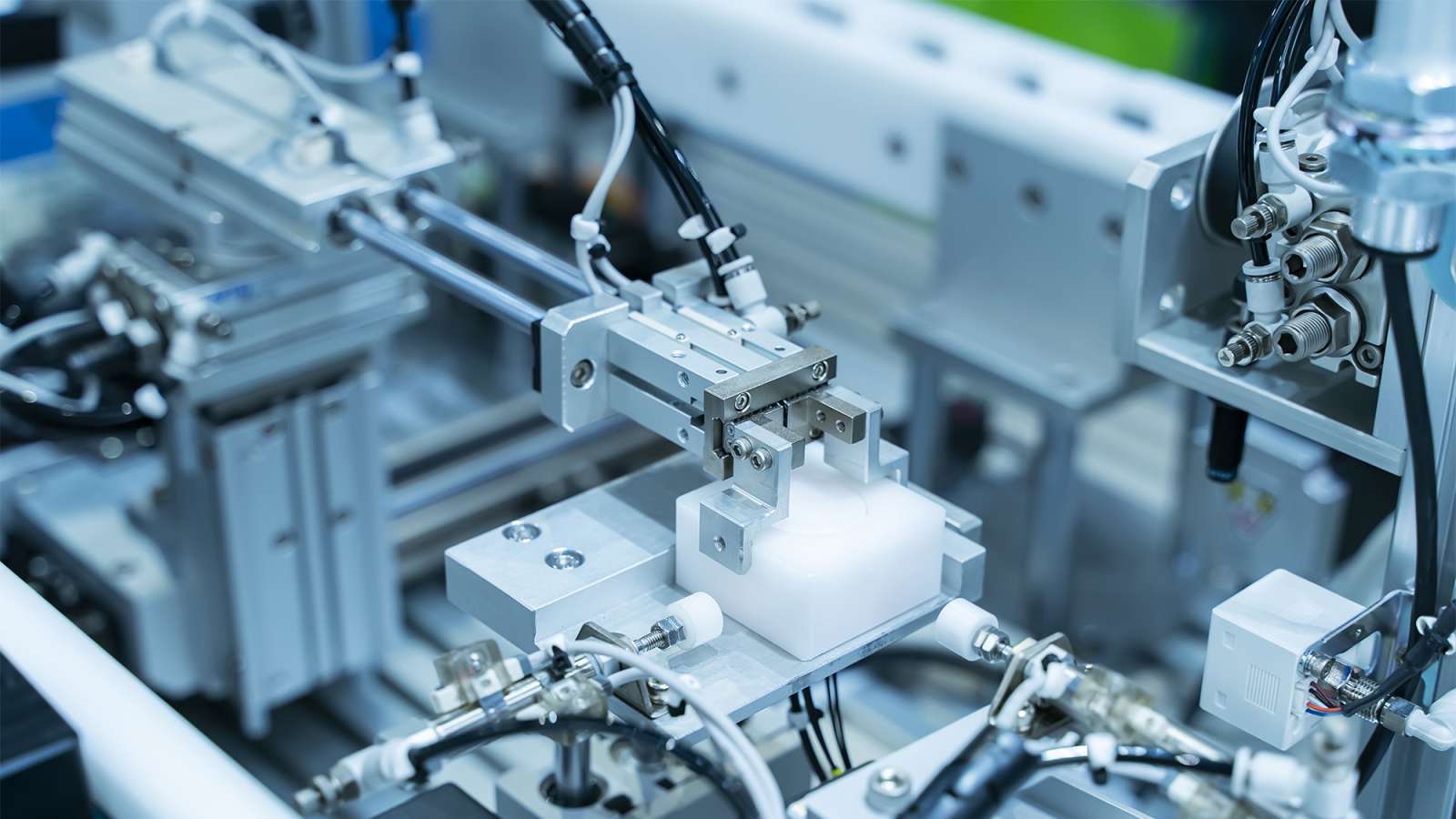 A machine with a robotic arm is gripping a rectangular cube on a small metal platform.