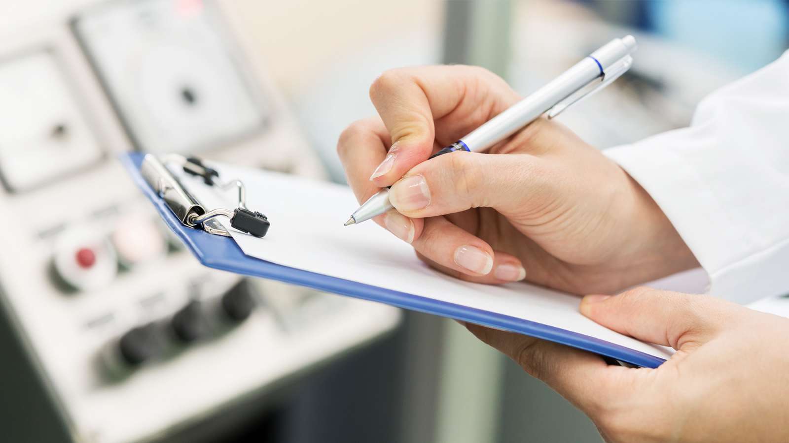 A close up view of an engineer holding a clipboard and a pen writing down notes in front of a machine.