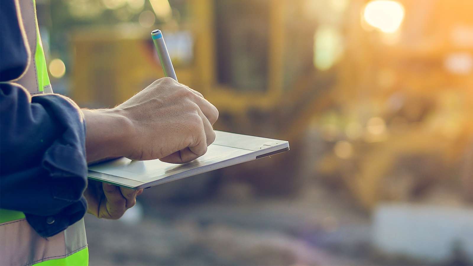 An engineer wearing a safety vest uses a tablet to inspect a construction site.