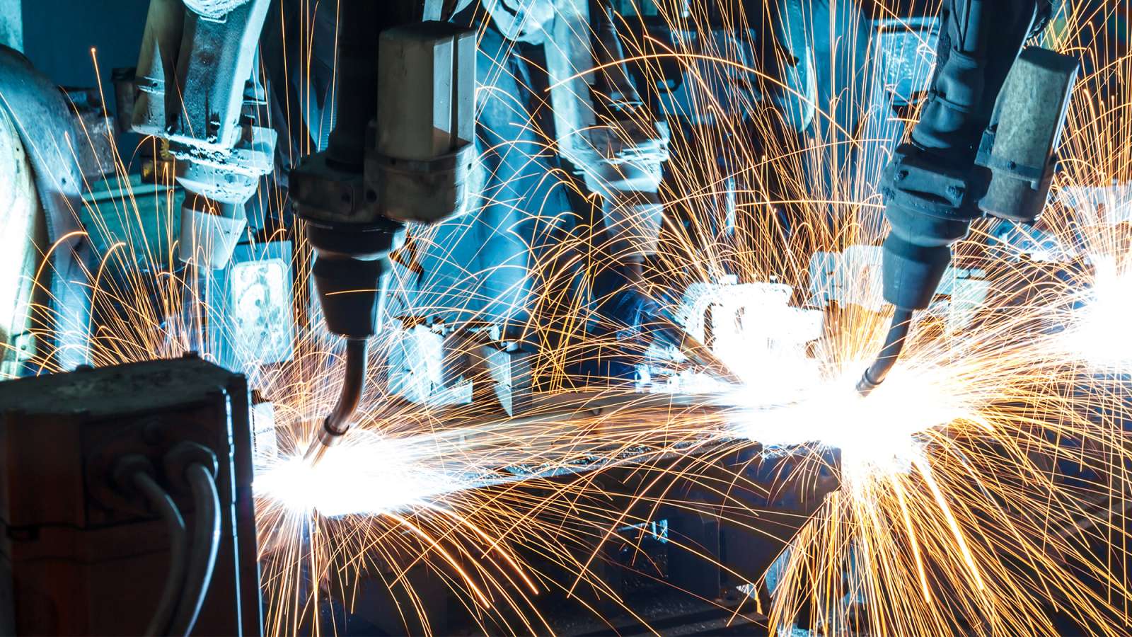 Several robotic arms are welding auto parts inside of an automotive factory.