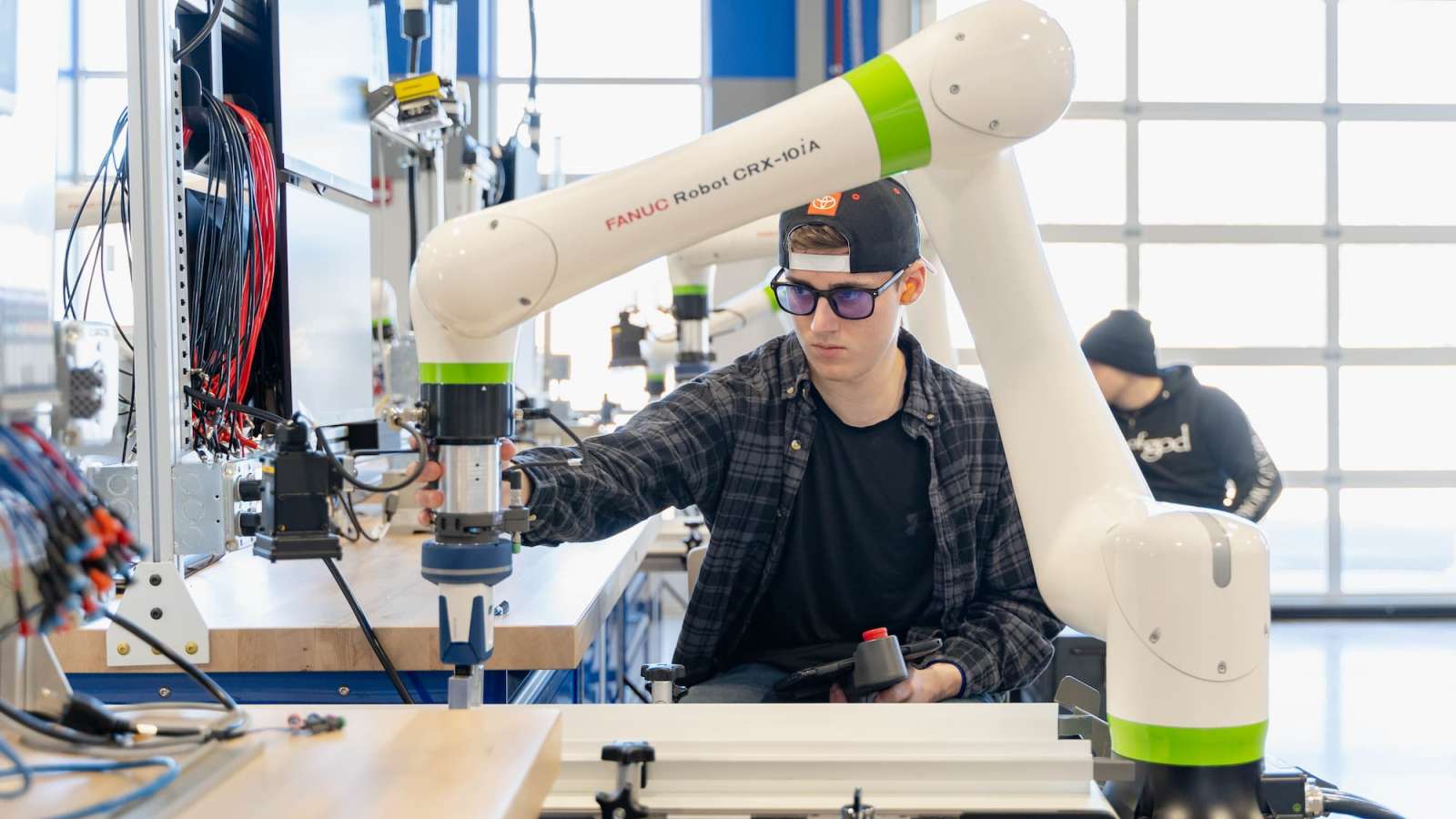 A student prepares and manually adjusts the position of a smart manufacturing robot.