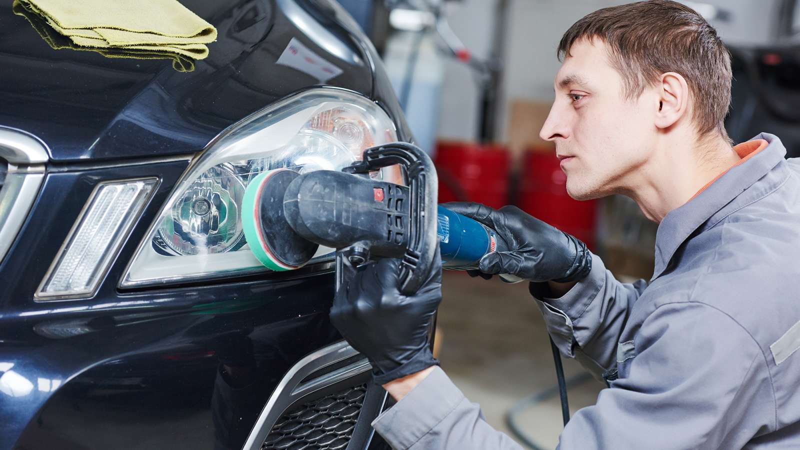 An auto repair person is using a tool to polish the headlight of a vehicle.