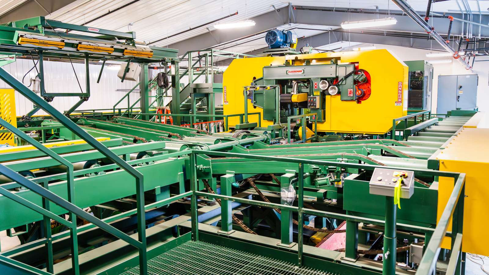 Wide-angle view of Northcentral Technical College’s sawmill facility, showcasing a large yellow Cleereman bandsaw, green conveyors, and integrated log scanning and control systems.
