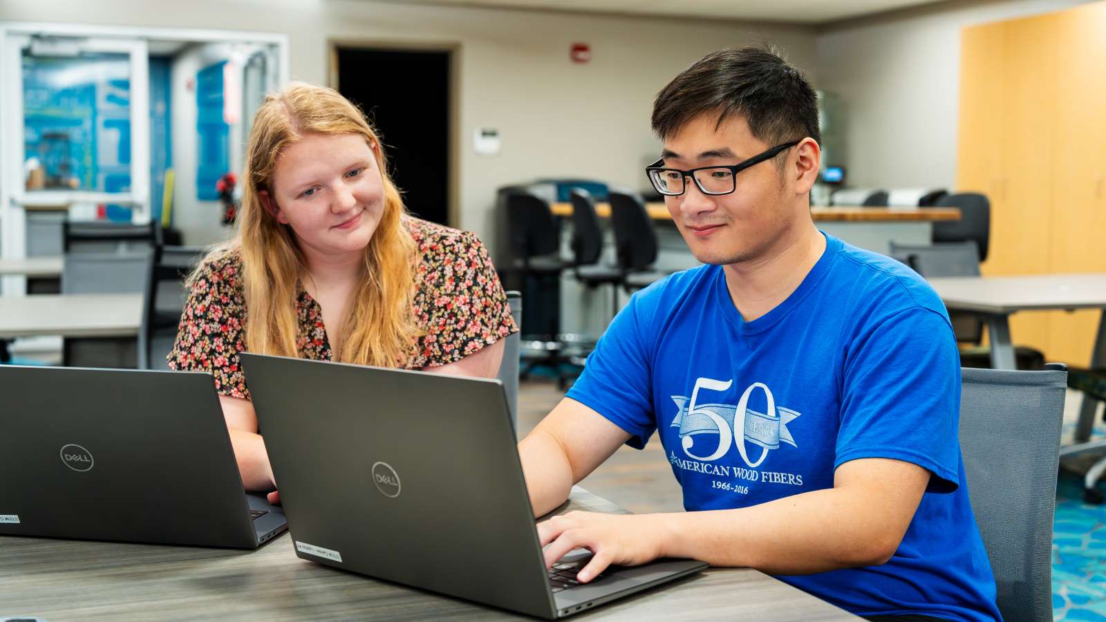 A prospective student types on his laptop at a table, while a member of the NTC staff smiles, looking on as he completes his admissions requirements..