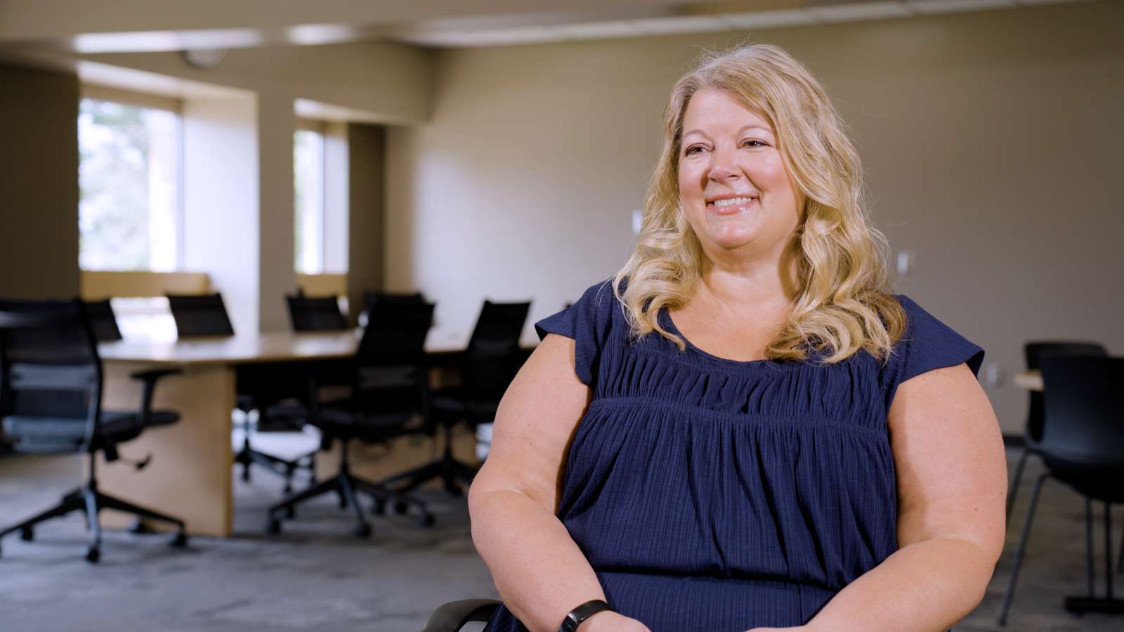 Amy sitting in a modern conference room, wearing a dark blue top.