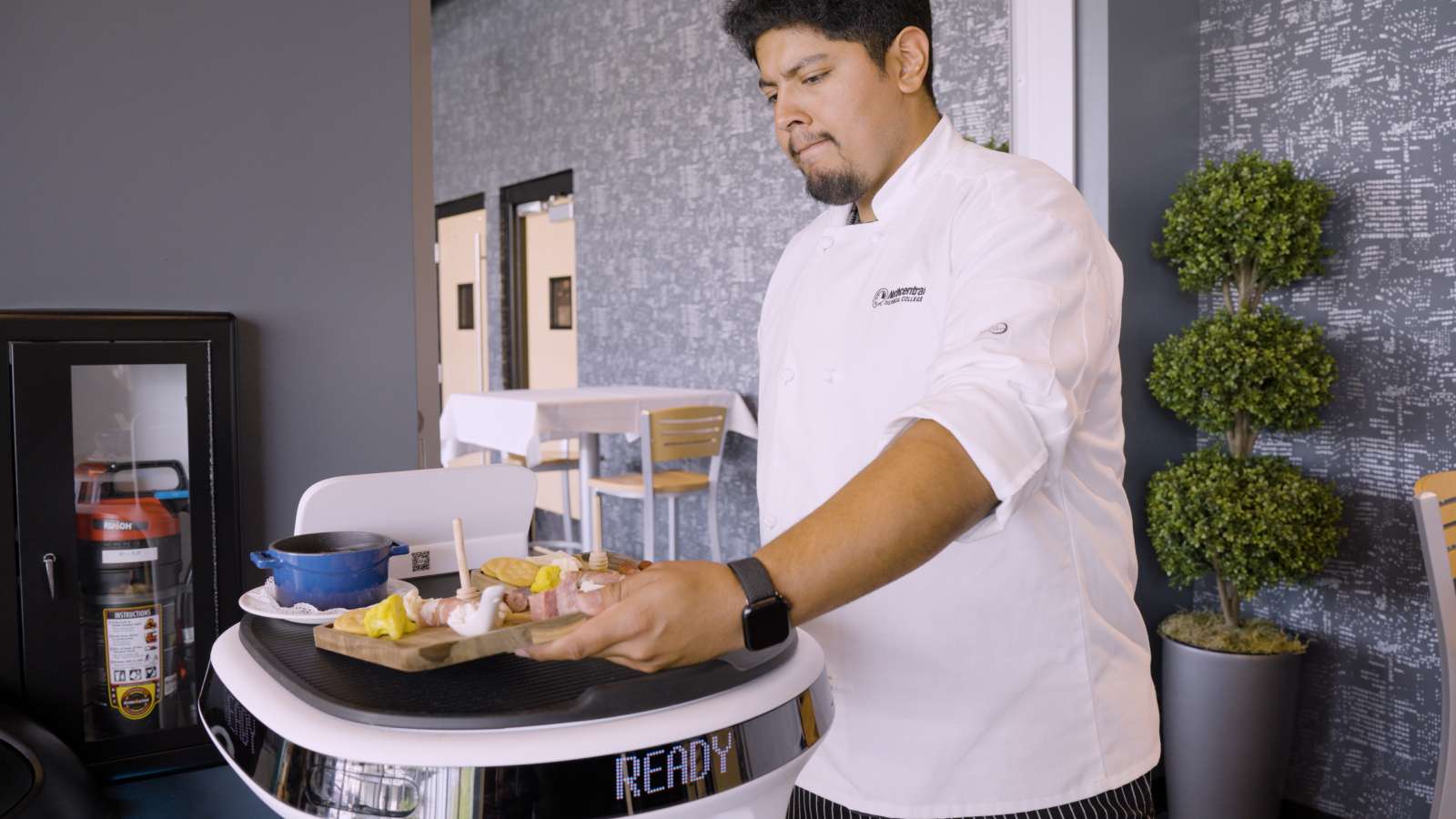 A culinary student serving food with help from an AI robot.