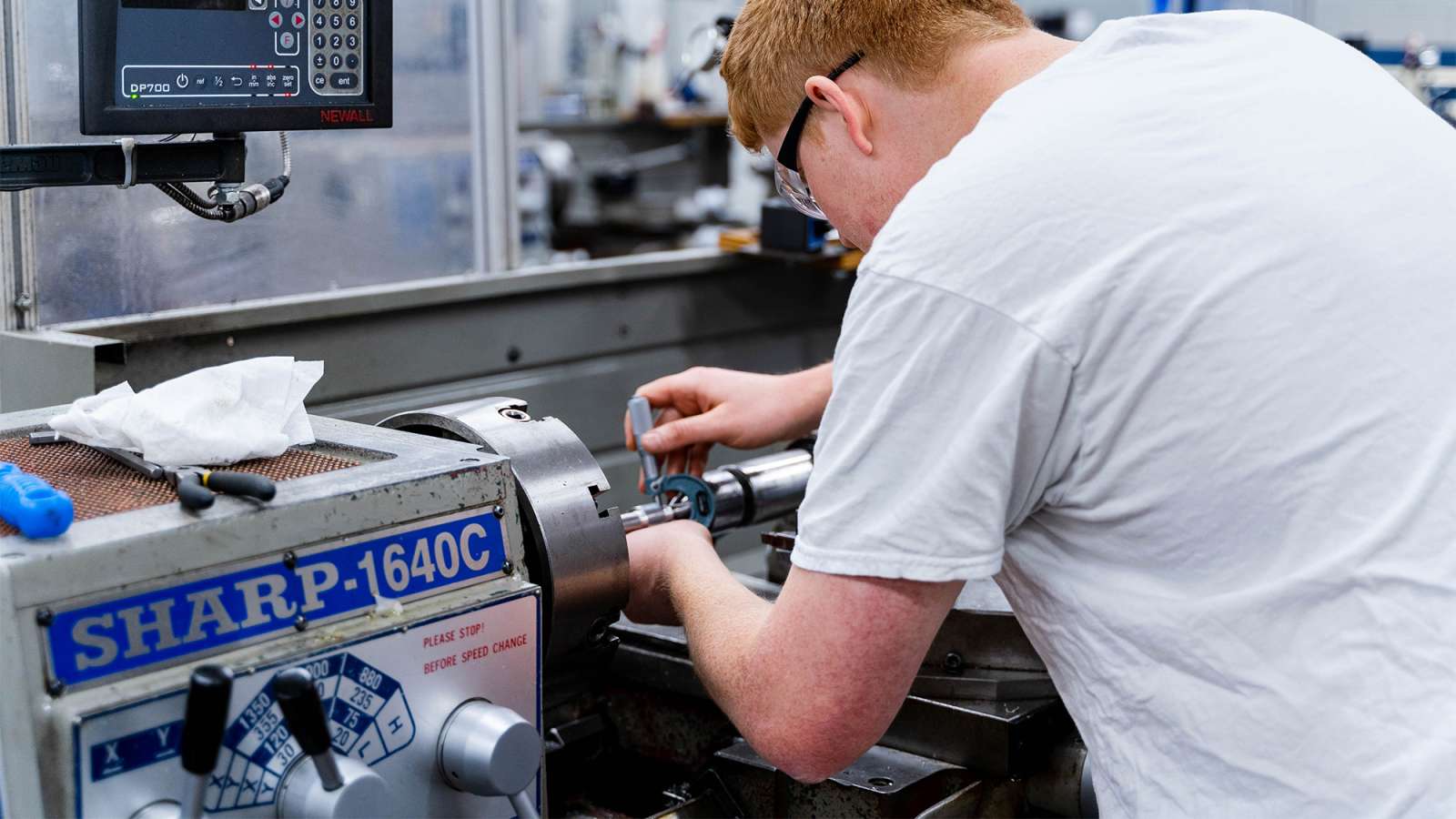 Technician in white t-shirt working on a stainless-steel commercial Sharp ice machine in a busy kitchen.