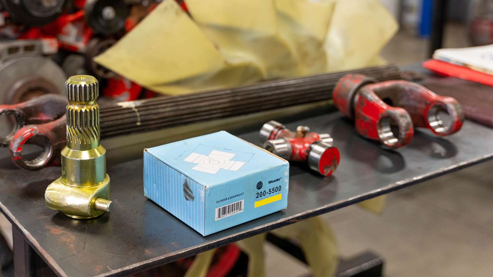 Metal workbench holding a gold splined shaft, small blue labeled module, and three red-handled sockets and tools.