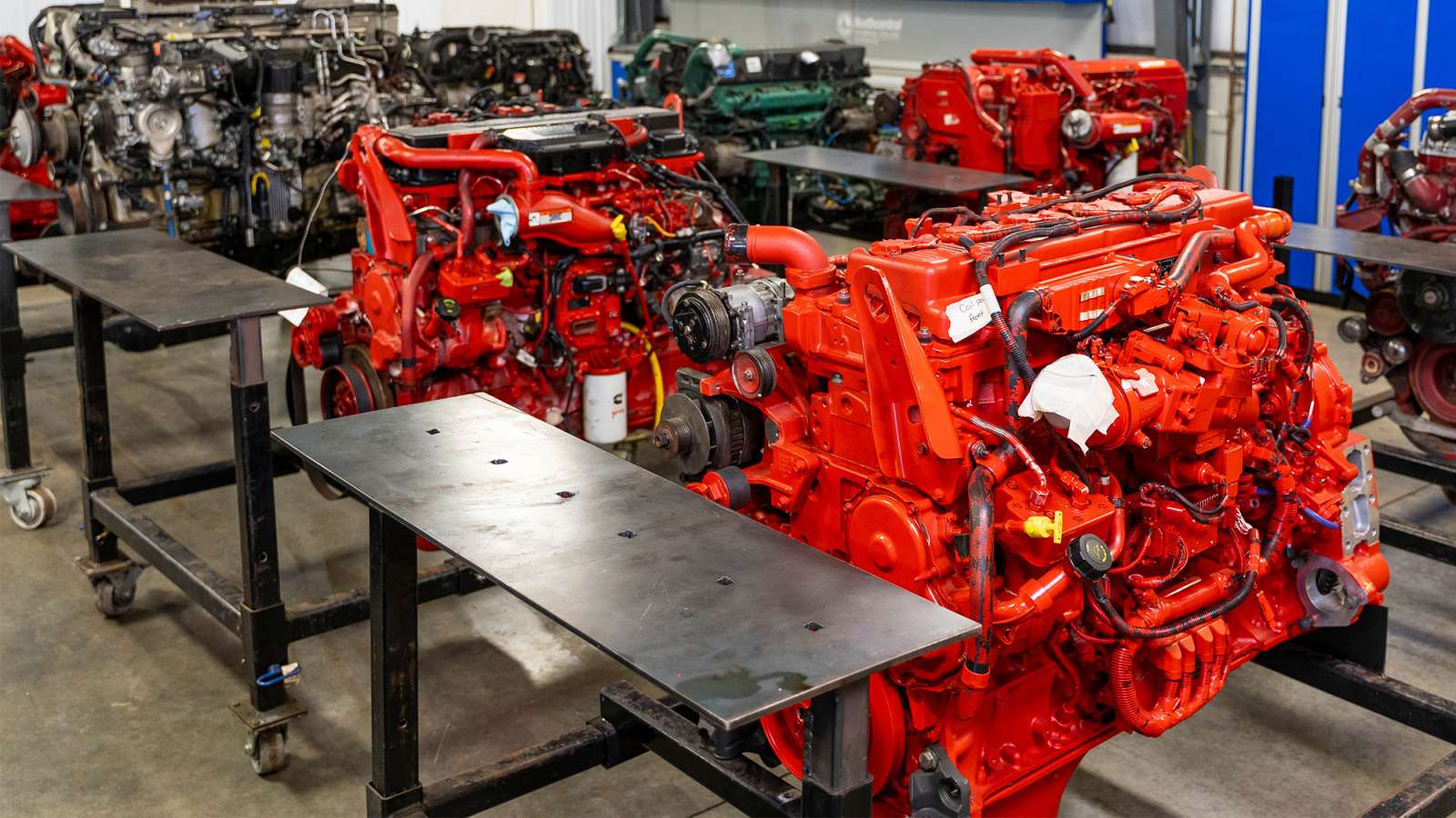 Bright orange-red industrial diesel engines lined on metal stands in a clean workshop with assorted engine parts.
