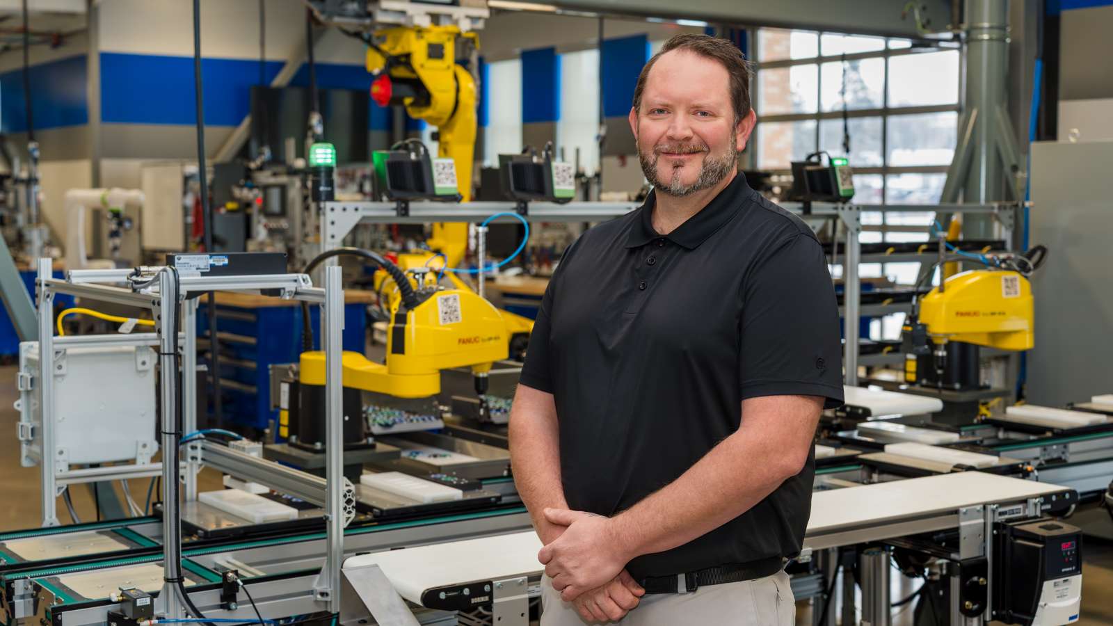 Dustin Van De Weerd smiling with arms crossed while standing inside the Industry 4.0 Smart Manufacturing Lab