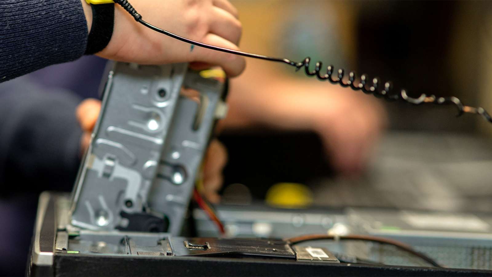 Technician's hands installing a metal hard drive into an open desktop computer, coiled cable and circuit boards visible.