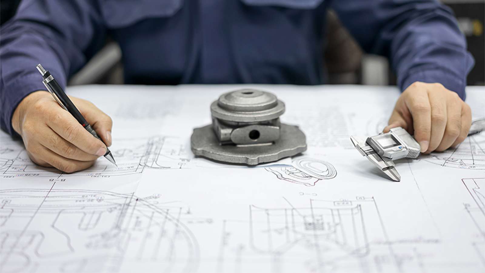 Engineer in blue jacket marking technical blueprints with pen.