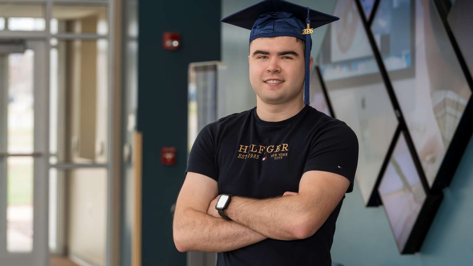 Mick smiling while wearing his graduation cap and his arms crossed.