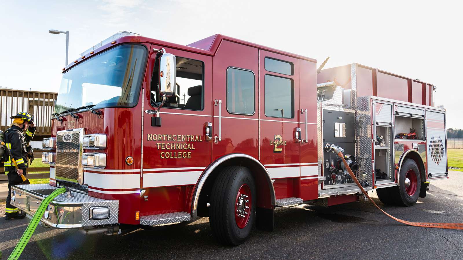 a red fire engine parked on pavement with hoses laid out and a firefighter standing nearby.