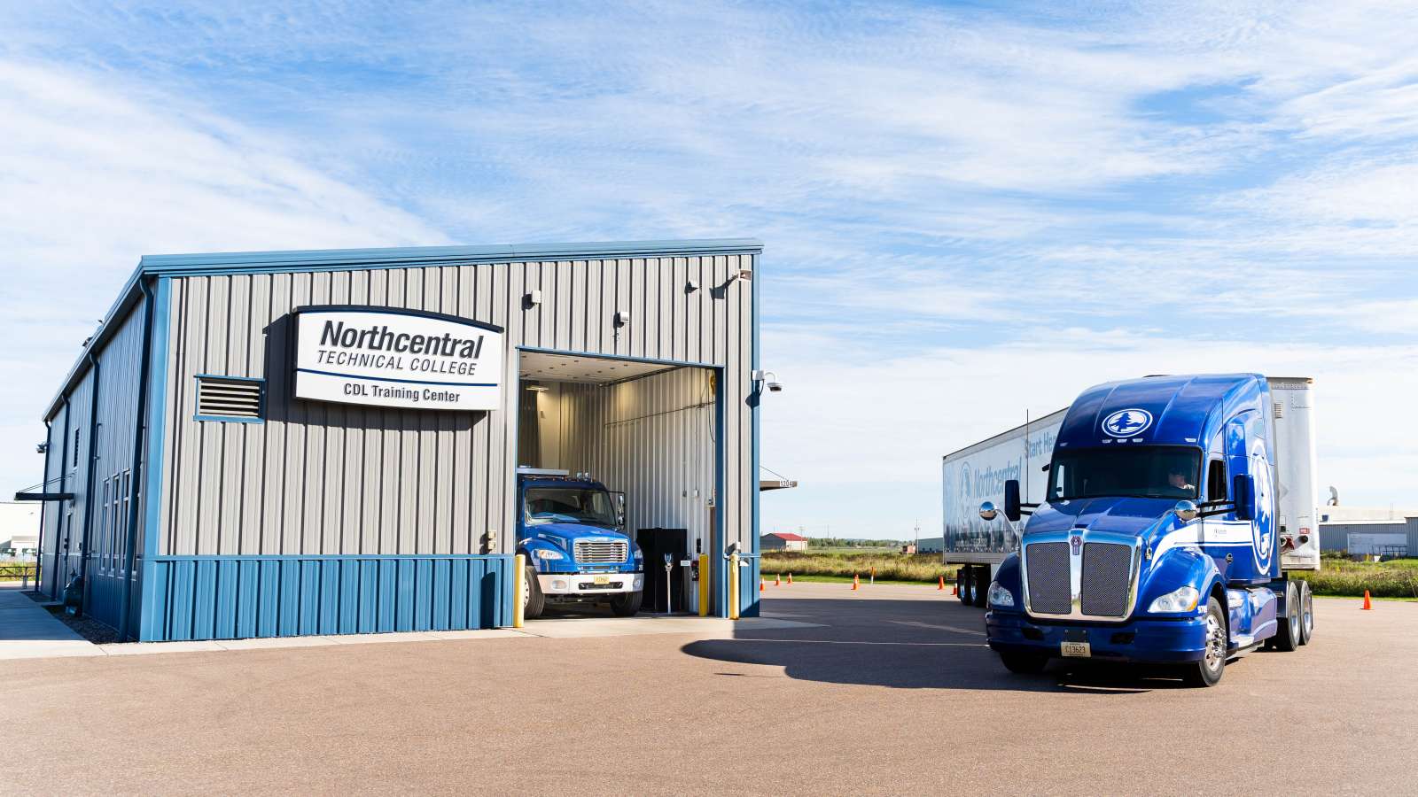 An NTC truck pulling around the front of the CDL Training Center, while another truck sits in the open bay.