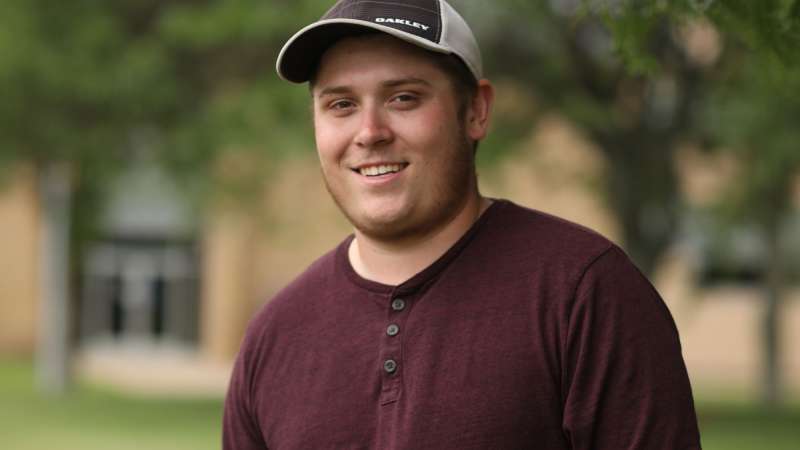 A student with a white and blue hat and a red long-sleeved shirt in the Wausau Campus Courtyard