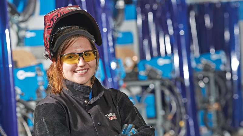 Welding student with her mask lifted over her head posing for portrait
