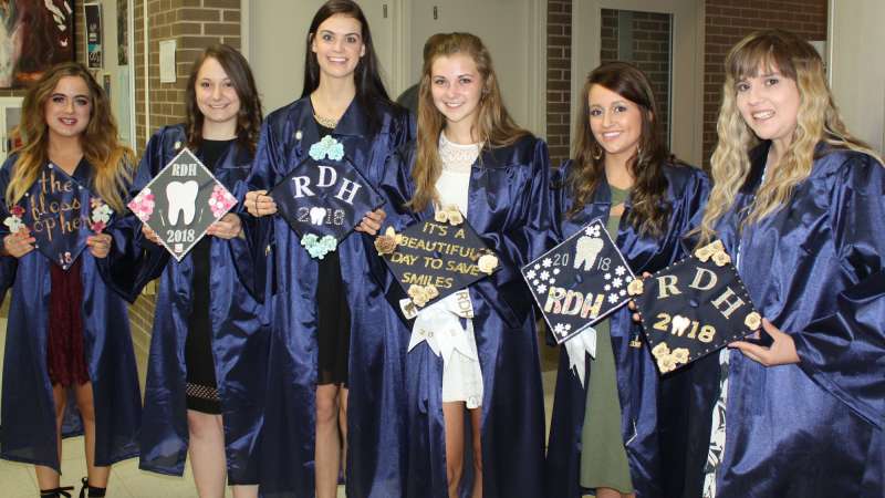 Six graduating students stand together holding their graduation hats