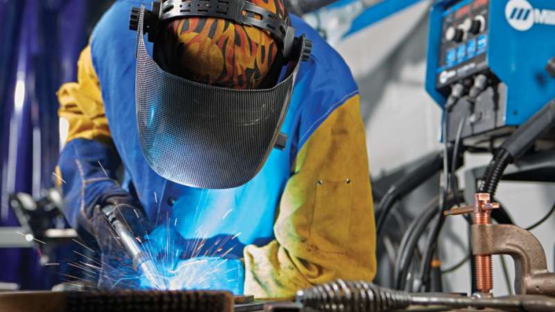 A student is looking down at objects he is welding together. Bright sparks are shooting from the objects