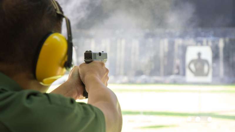 A man wearing ear protection points his gun at a target in the background.