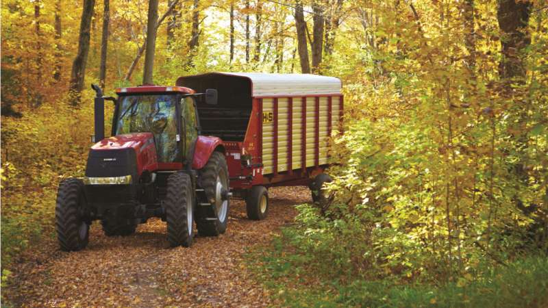 A tractor with trailer is driving slowly through the forest in Fall