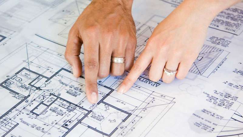 Two people point at a bedroom in blueprints.