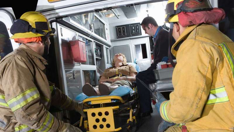 Two firefighters observe a female patient who was loaded into an ambulance.