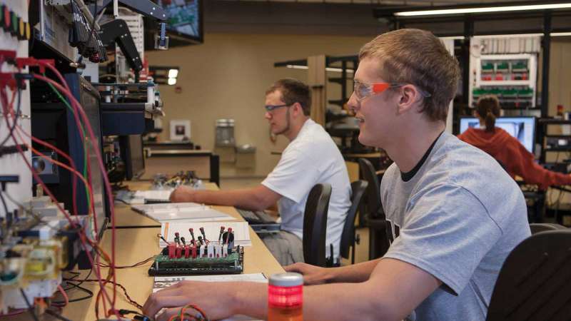 Two students sit at a table while they work on an electromechanical technology project.