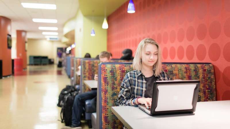 Student sitting at booth while typing on laptop