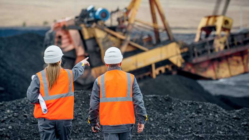 Two workers in blaze orange vests survey a site.